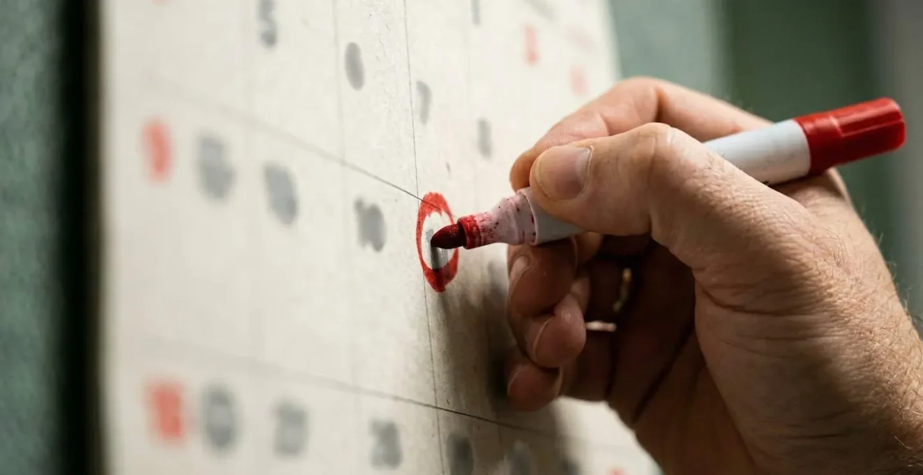 Main marquant une date d'échéance sur un calendrier avec un marqueur rouge